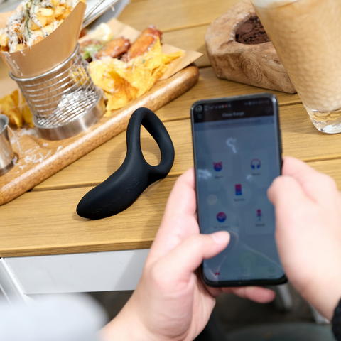 LOVENSE Diamo remote-controlled penis ring with smartphone app, featured on a table next to a meal.