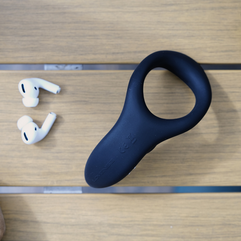 LOVENSE Diamo remote control vibrating ring on a wooden surface next to wireless earbuds.